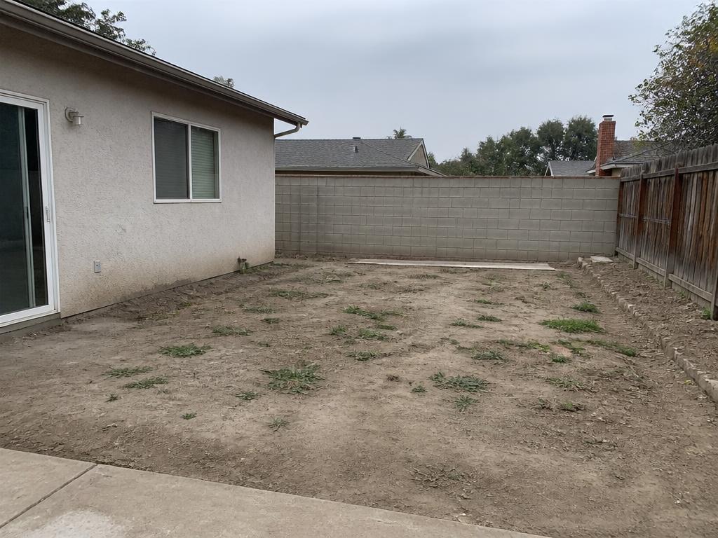 Bare dirt backyard with sparse weeds before landscaping